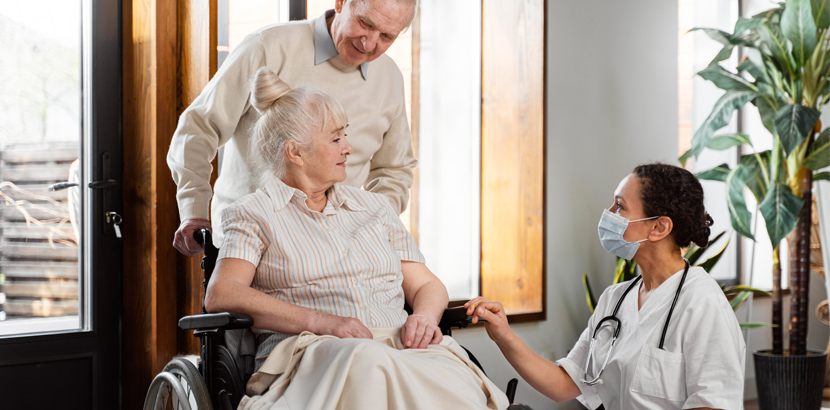 Caregiver assisting elderly woman in wheelchair, with supportive family member present, in a warm home environment, emphasizing in-home care and senior support services.