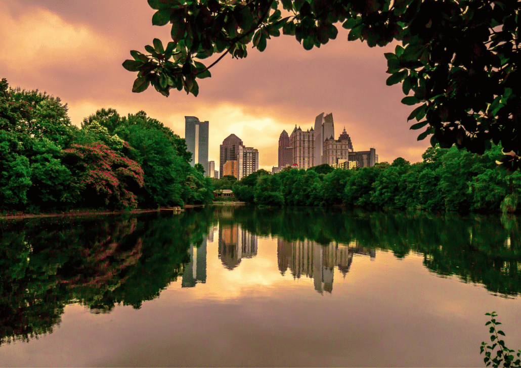 City skyline of Atlanta, Georgia reflecting in a serene lake surrounded by lush greenery and trees at sunset, illustrating a peaceful environment for seniors.