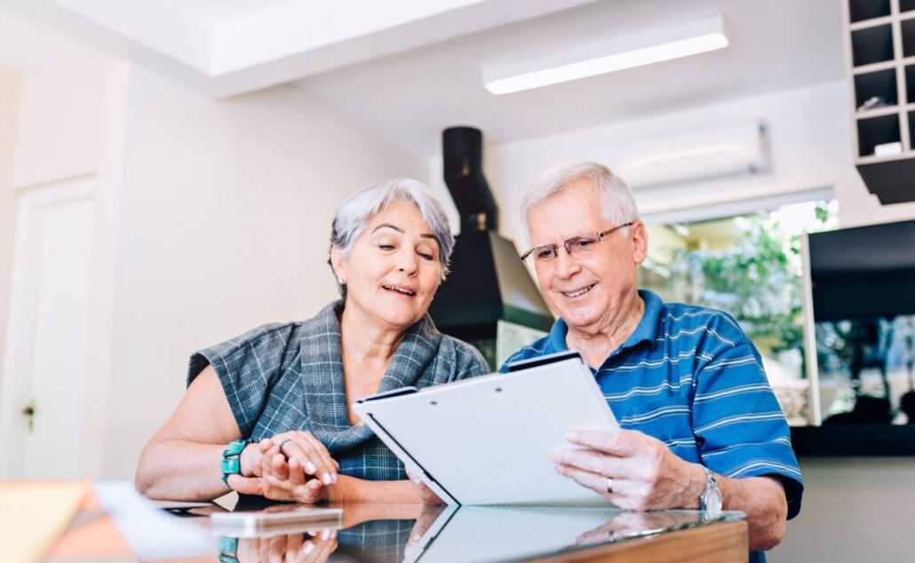 Older couple discussing financial planning while reviewing documents at home, emphasizing retirement and budgeting strategies.