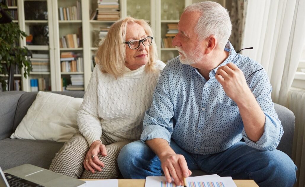 Elderly couple discussing financial planning at home, with documents and a laptop, emphasizing the importance of managing finances as they age.