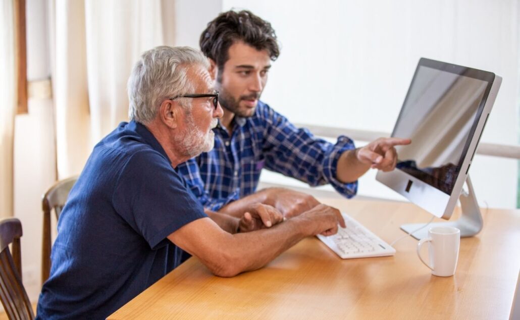 Young Man Teaching Elderly How to Use the Computer