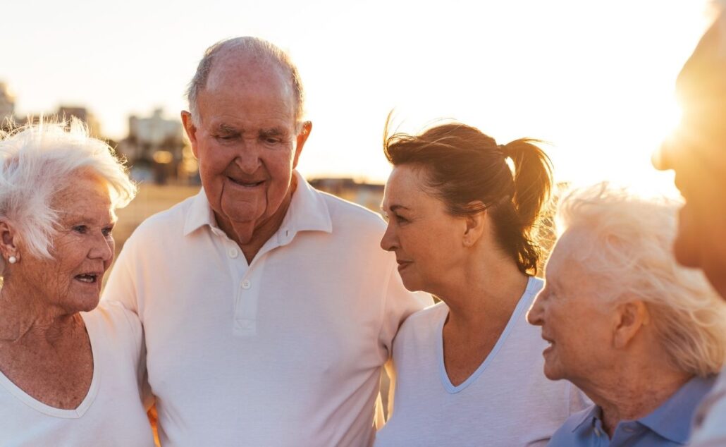 Group of seniors and a caregiver engaging in conversation during sunset, promoting community and support in aging.